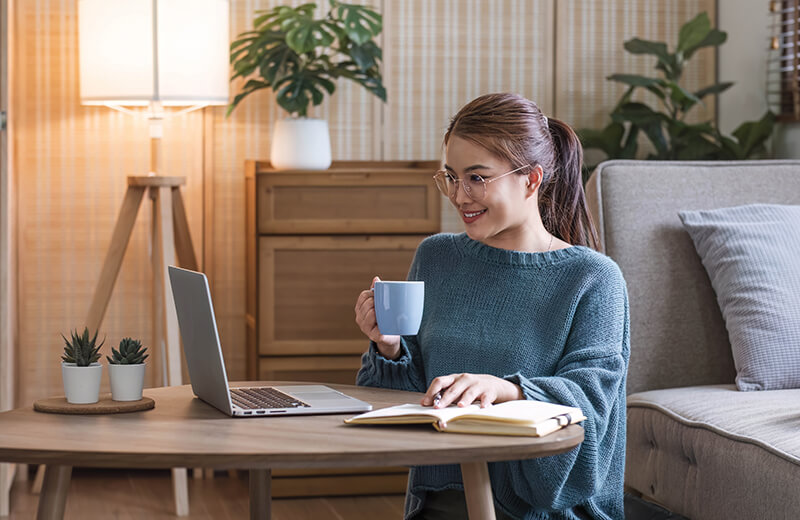 a woman drinking out of a mug and working on a laptop
